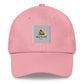 A pink dad hat with a sun and beach logo embroidered in light blue and yellow on the front. The hat is made of light-colored cotton fabric and has a curved brim. It has an adjustable strap at the back for a comfortable fit."